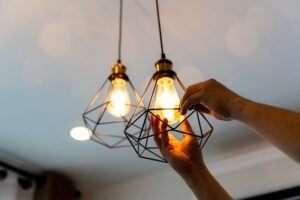Electrician Kansas City Fusion Electric AdobeStock_575840573 Electric LED Lightbulb Change In Light At Home. Decorative antique edison style filament light bulbs hanging. An electrician is installing spotlights on the ceiling