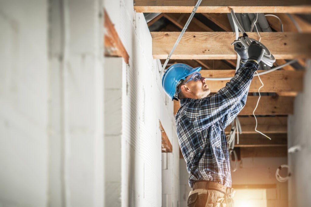 Professional Electrician Working on Electrical Wiring System Installation in New Residential House Ceiling.